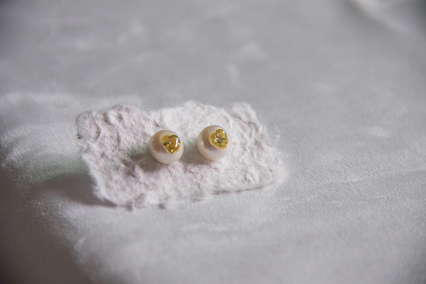 Close-up view of natural freshwater pearl stud earrings with yellow zircon heart charm and sterling silver backing