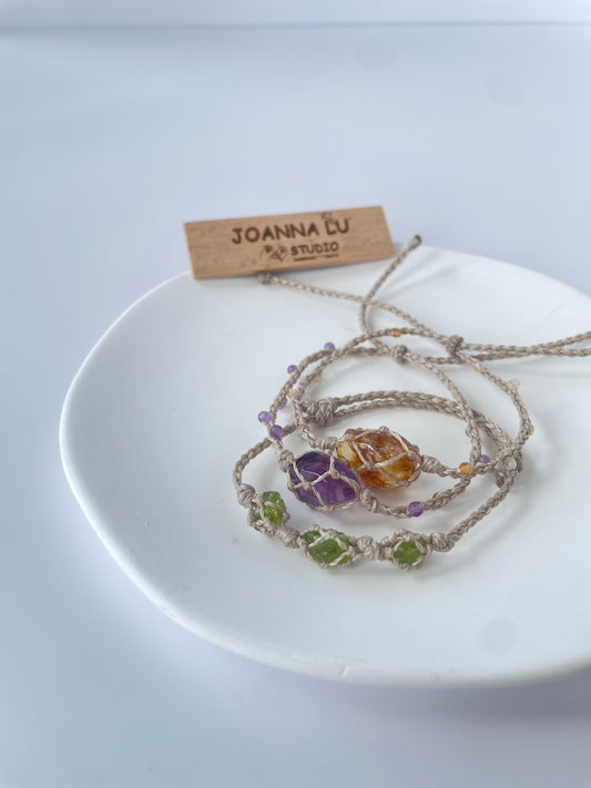 Handmade crystal healing bracelet with Peridot, Amethyst, and Citrine on adjustable wax cord displayed on white plate.