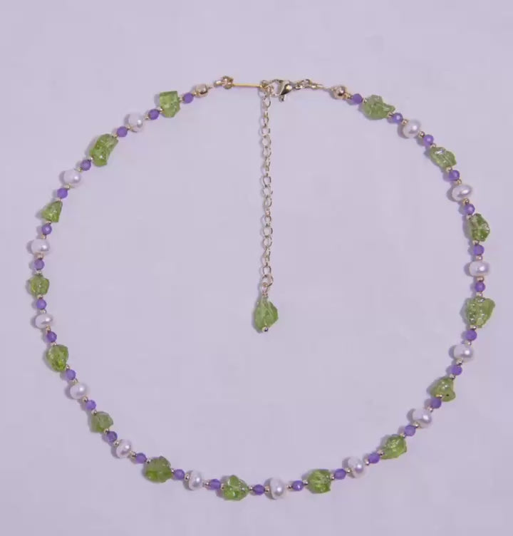Side view of nature-inspired necklace showcasing vibrant green and purple gemstones with pearl details